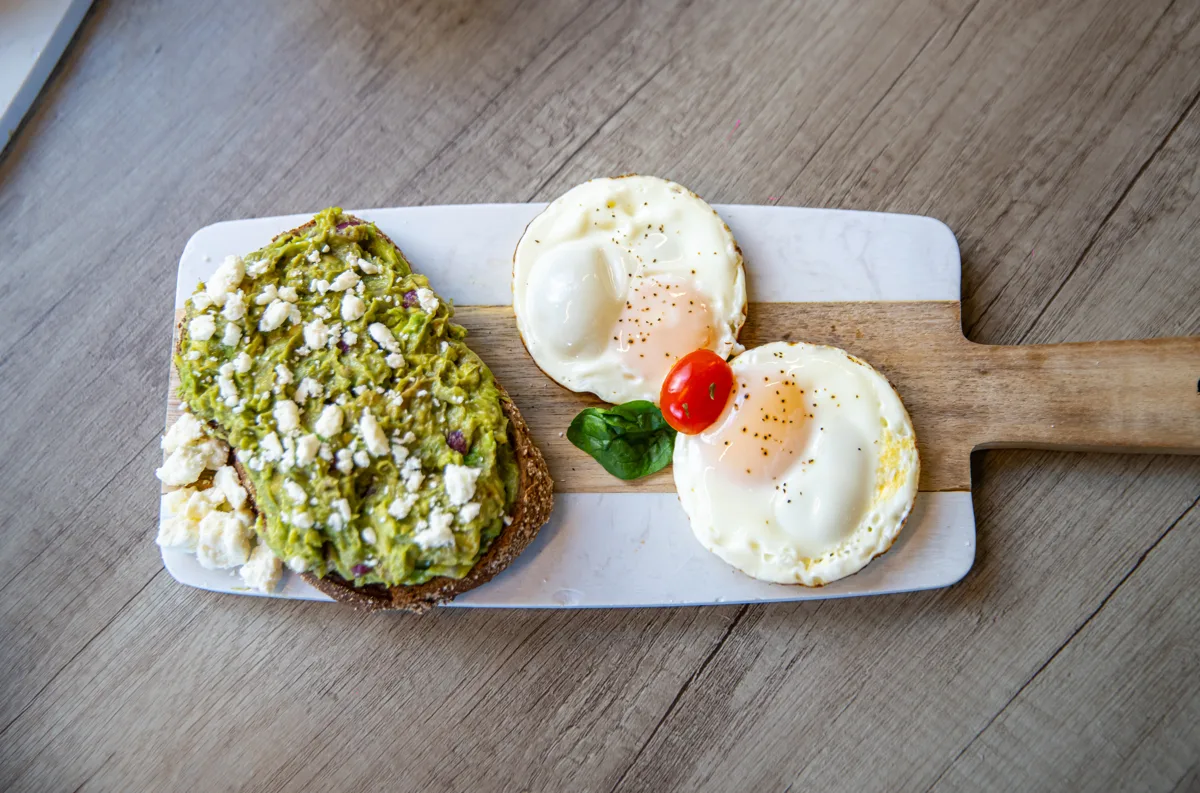 Avocado toast with feta and eggs on a wood board