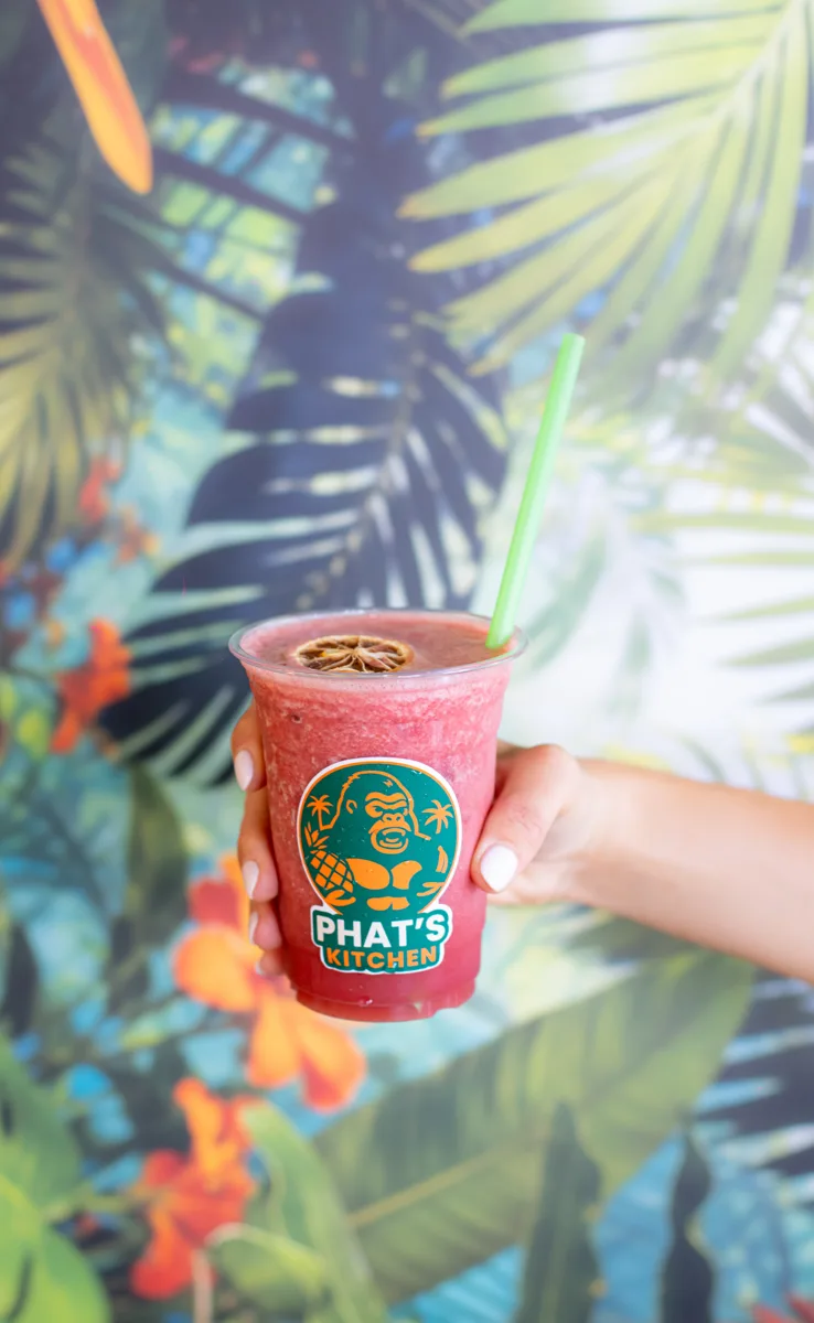 Berry Glow energy refresher held up against the tropical mural at Phat's Kitchen